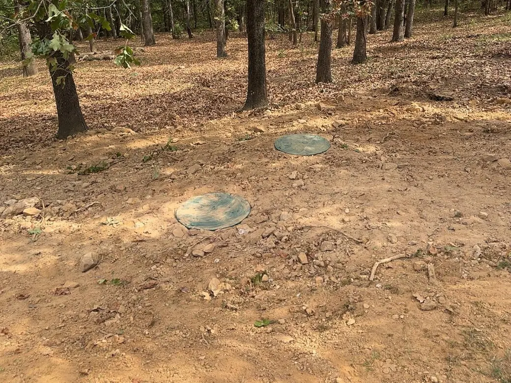 Two septic tank lids at grade on a wooded lot, aerobic septic system maintenance