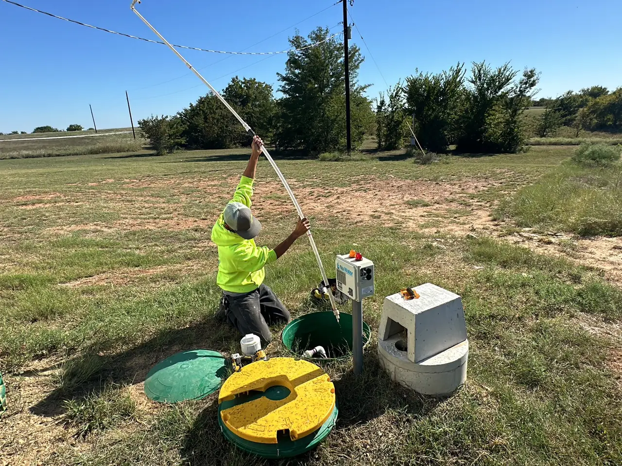 Technician kneeling at an open aerobic septic system beside the control panel and compressor cover, aerobic septic system repair