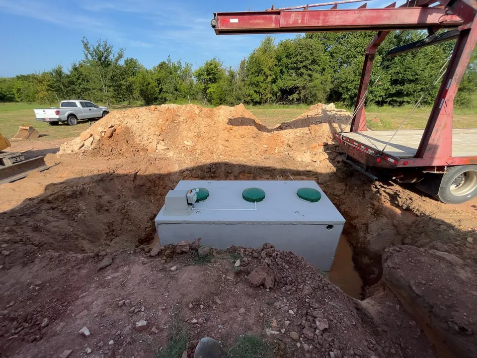 Concrete aerobic unit with green lids and a control box set in a fresh hole with a boom truck behind it, aerobic septic system repair