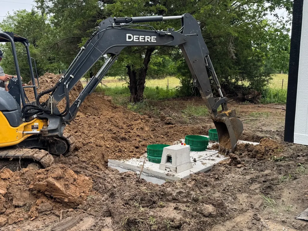 Excavator backfilling around new aerobic system risers and a concrete cover, aerobic septic systems