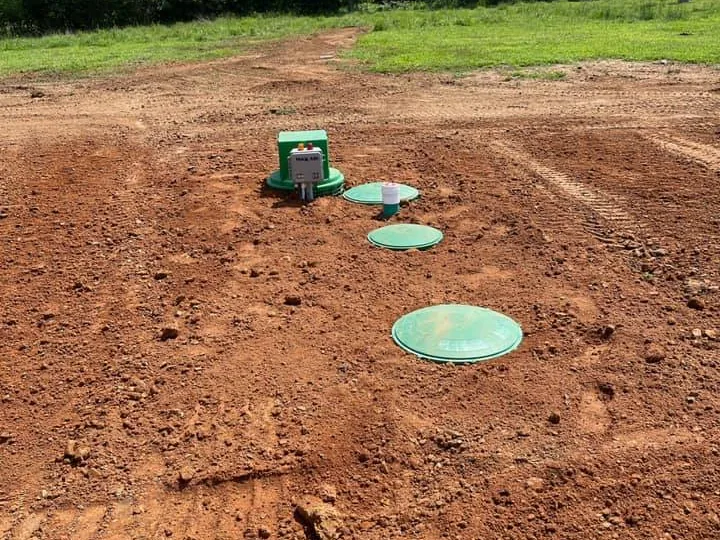 Finished aerobic septic system with three green lids and a control panel on fresh red dirt, aerobic septic systems