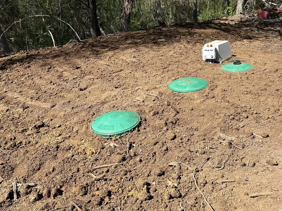 Green tank access lids and a control panel at grade in fresh dirt, septic inspections