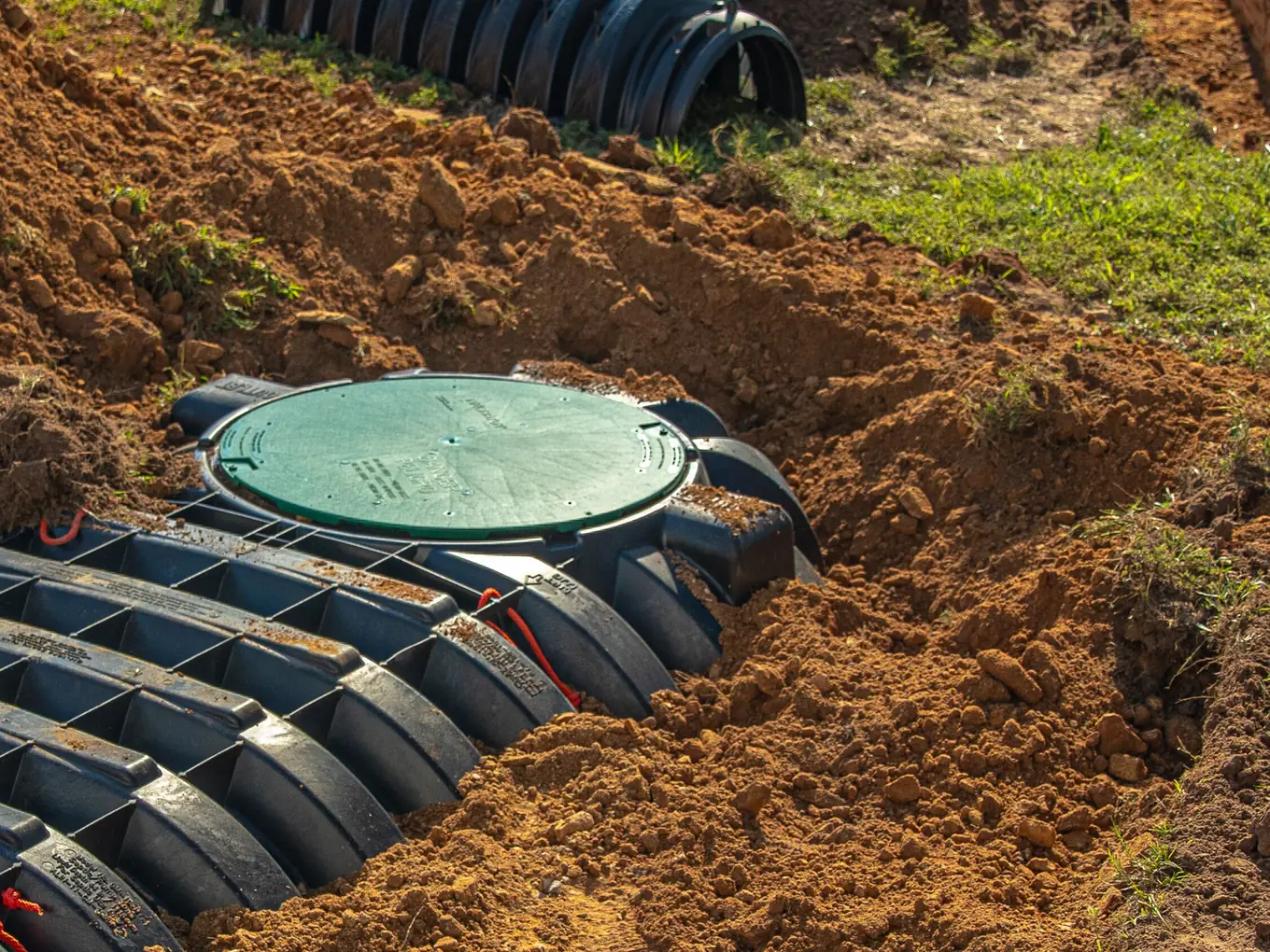 Green access lid on a plastic septic tank beside lateral line chambers, septic inspections