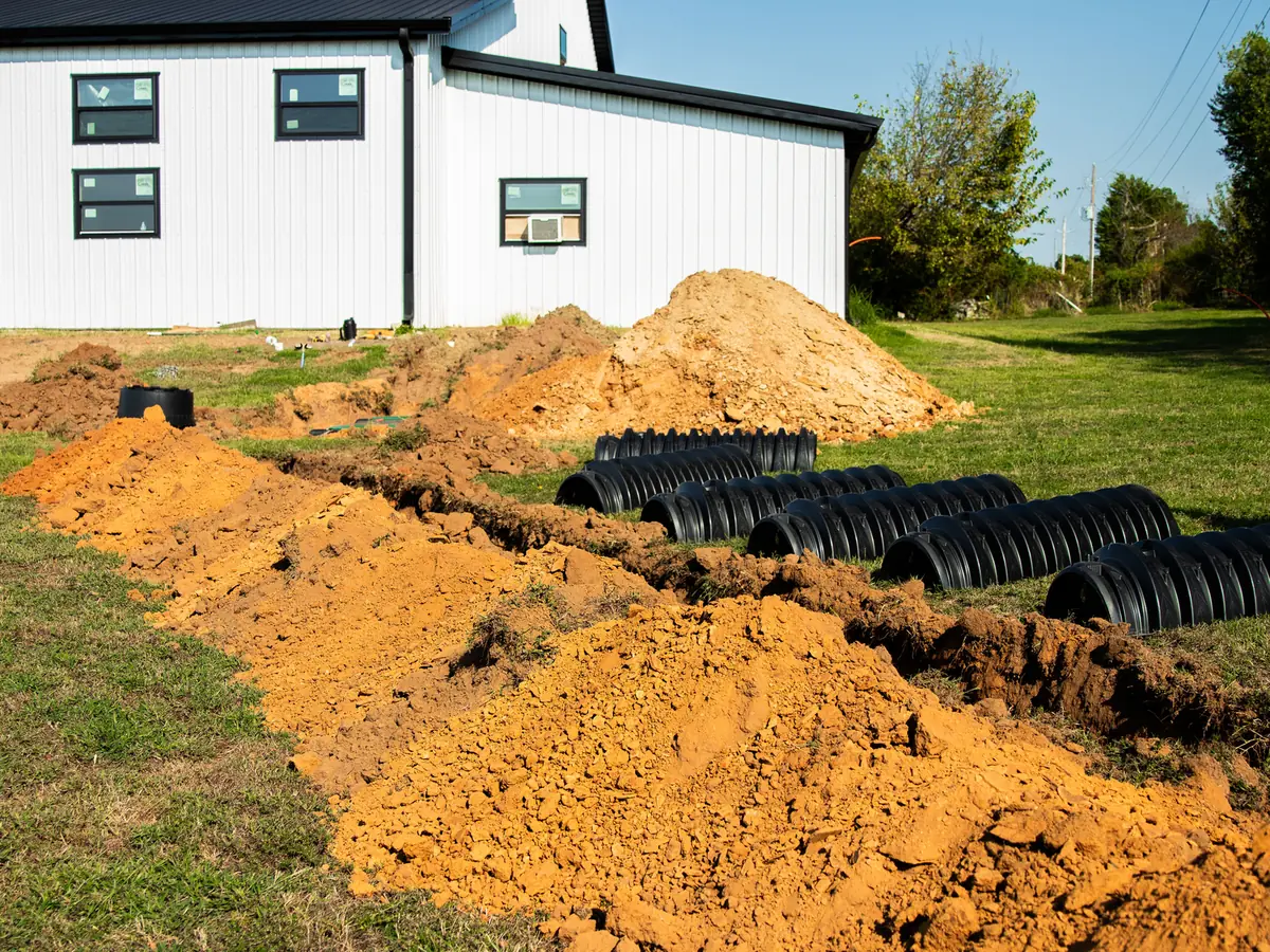 Lateral line chambers laid out beside a fresh trench next to a new metal building home, septic system installation