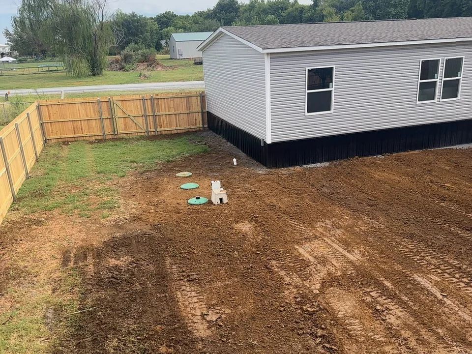 Finished septic system installation behind a manufactured home: a graded yard with the tank lids and aerator at grade, septic system installation