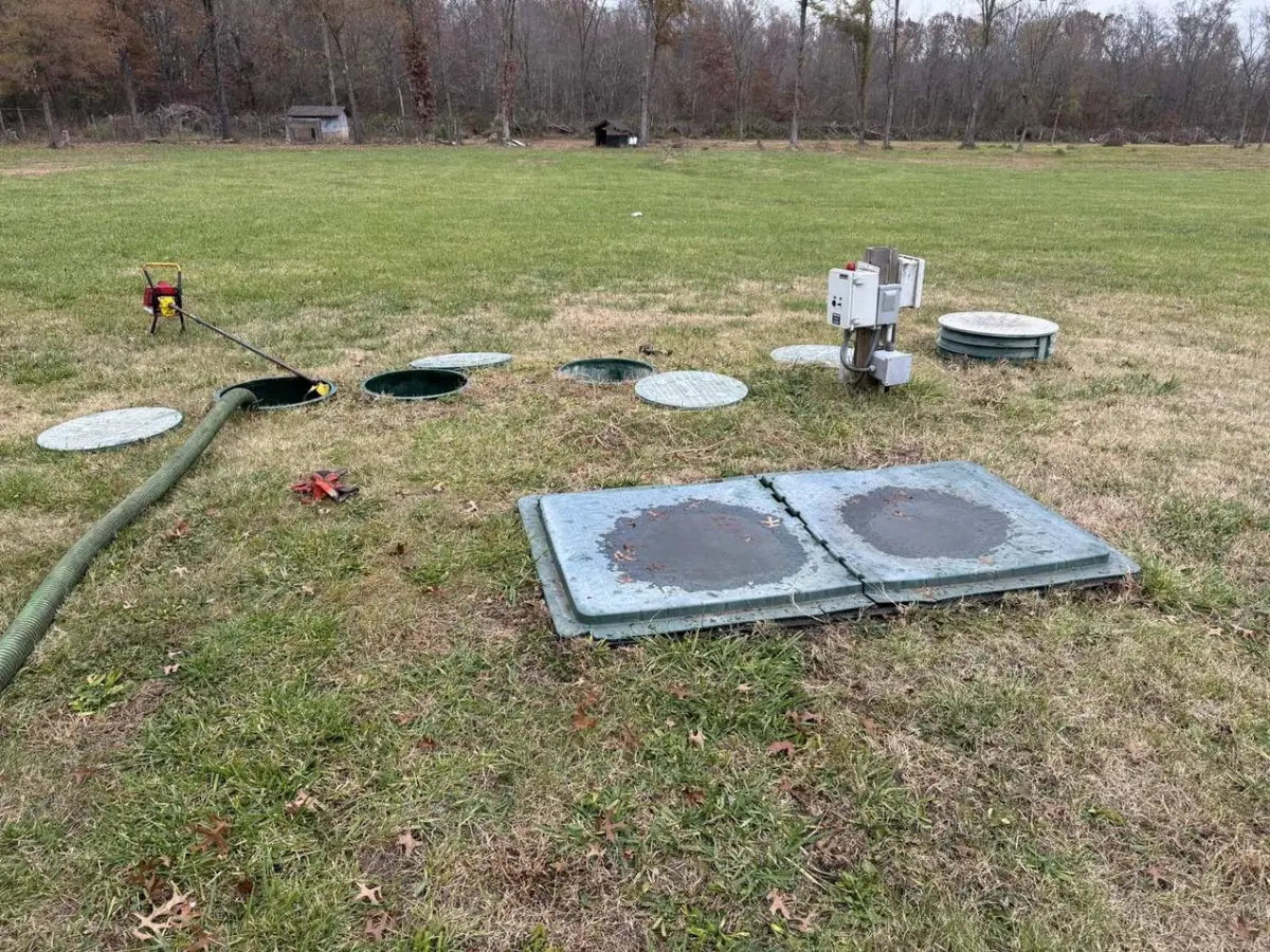 Septic tank lids off with a hose in one riser beside a control panel in a grass yard, septic system repair