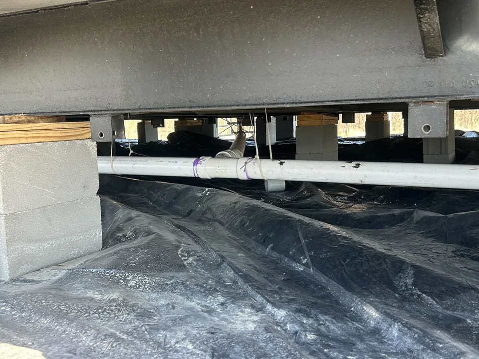 New PVC sewer line run under a home on piers over fresh gravel and a vapor barrier, septic system repair