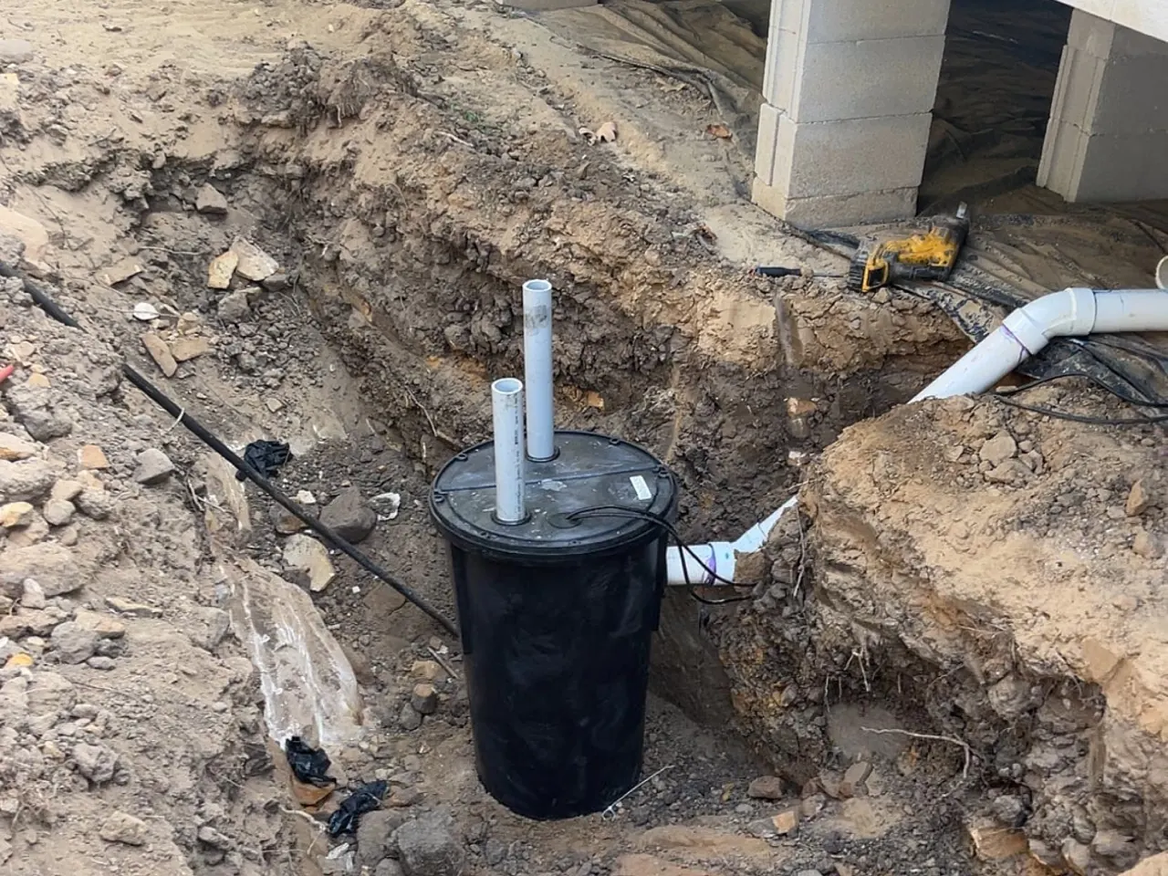 Black pump basin with PVC pipes set in a trench beside a home, septic system repair