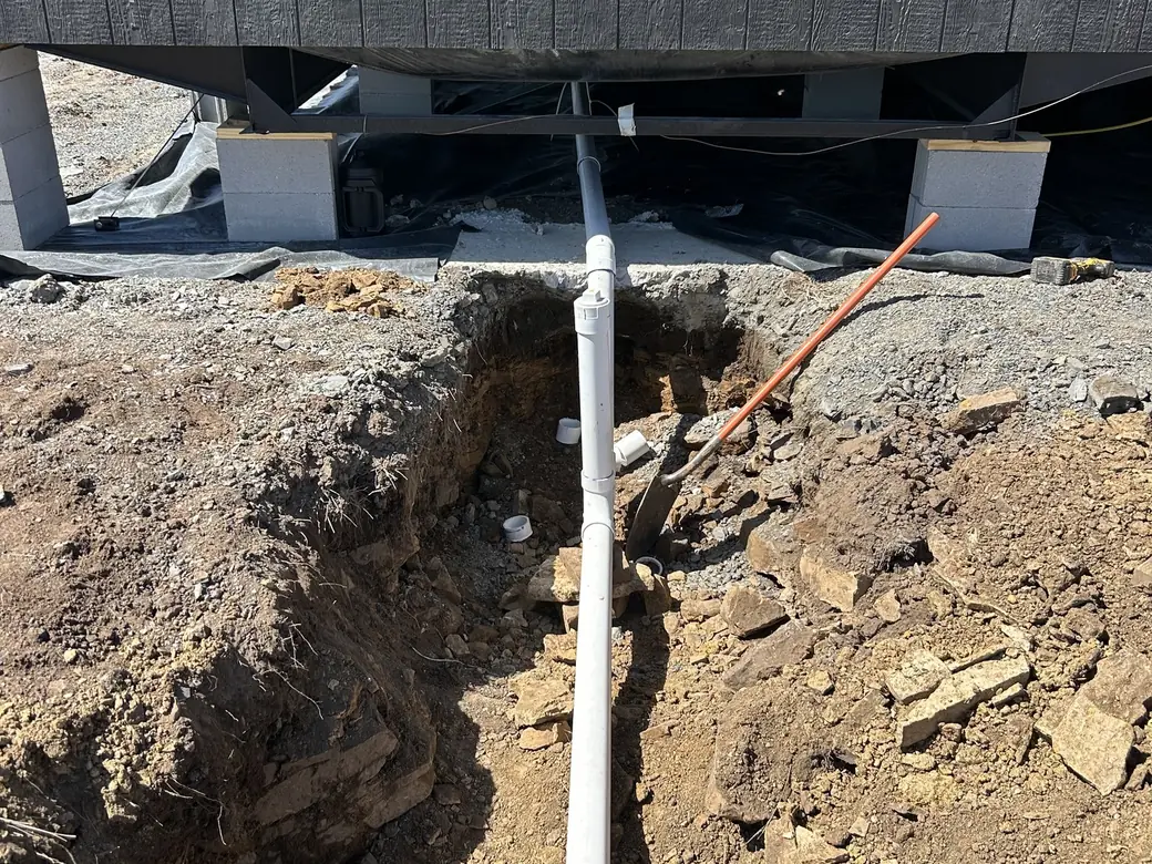 New PVC sewer line run from under a home into an open trench, septic system repair