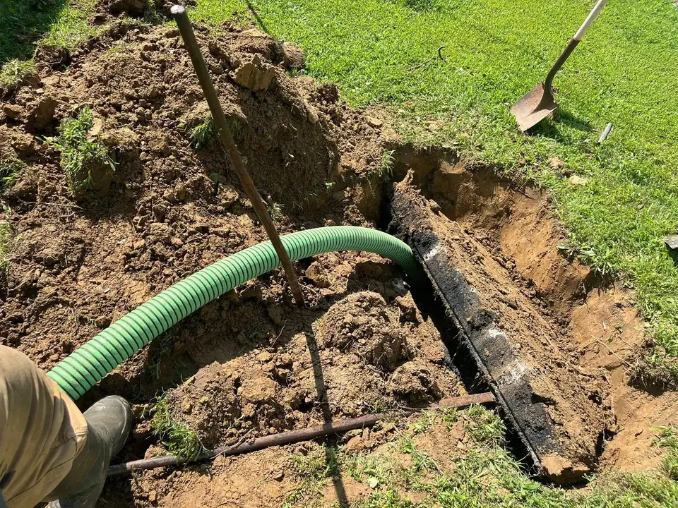 Green vacuum hose run into a dug out septic tank opening in a lawn, septic tank pumping