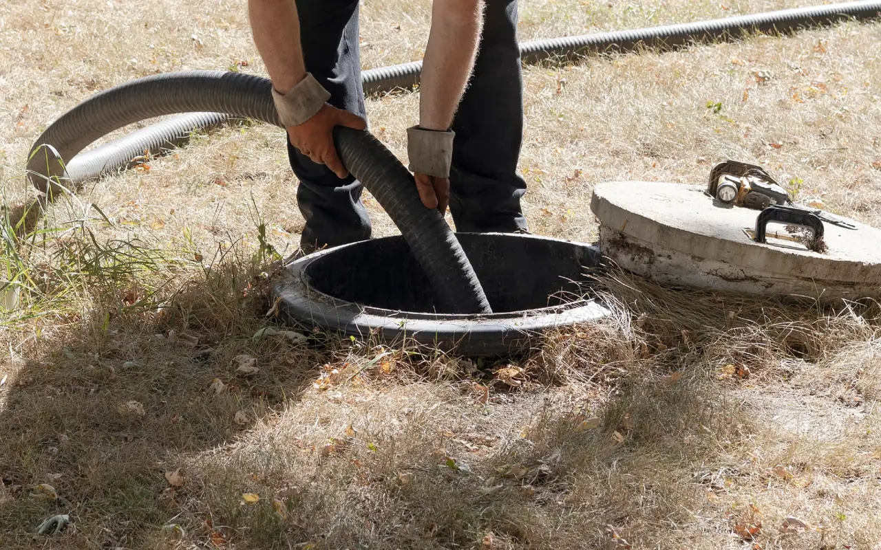 Worker feeding a vacuum hose into an open septic tank riser, septic tank pumping