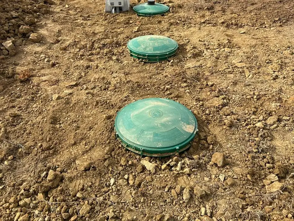 Two green septic tank riser lids at ground level in a dirt yard, septic tank pumping